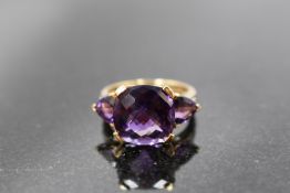A three stone heat treated amethyst ring having central facet cut stone flanked by two triangular