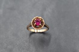 A ruby solitaire ring in a four claw setting in a flower style mount on a gold loop, marks worn,