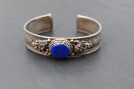 A white metal cuff bangle having moulded Asian style decoration and an inset Lapis Lazuli`