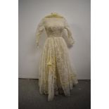 A late 1950s/ early 1960s lace wedding dress having full length sleeves and cowl neck, with bow
