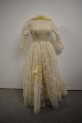 A late 1950s/ early 1960s lace wedding dress having full length sleeves and cowl neck, with bow