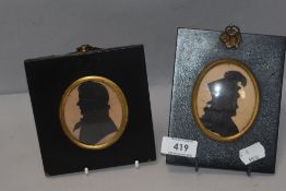 Two Victorian silhouettes of cut out design on black backgrounds with ebonised frames and domed