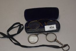 A pair of early 20th century fold away spectacles with a similar yellow metal framed pair