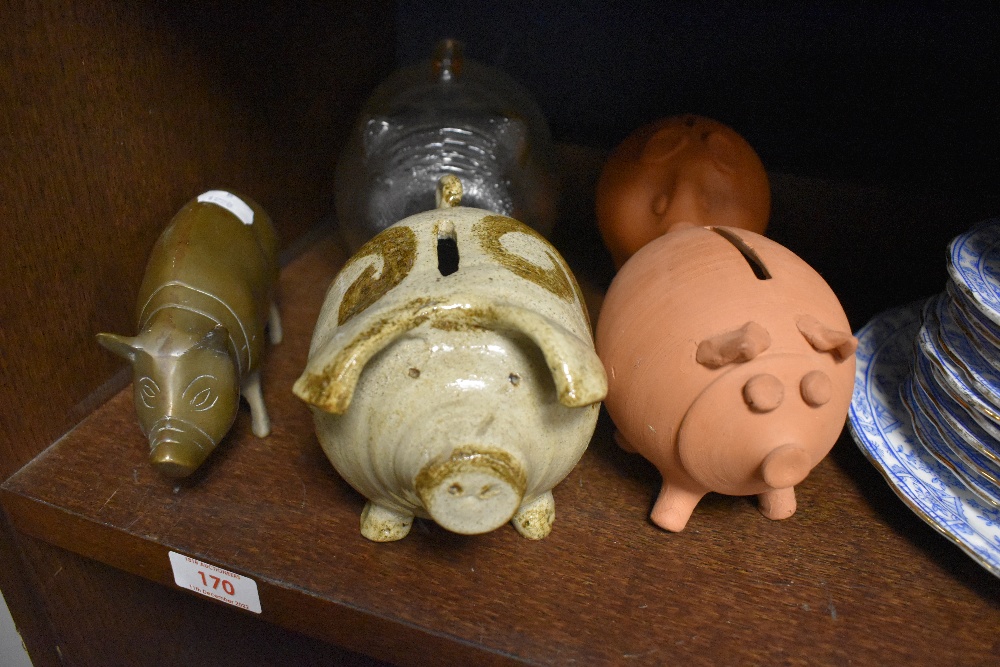 A group of four pig form money banks, comprising glass, glazed pottery and terracotta, and sold