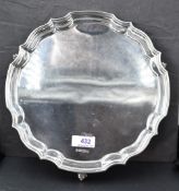 A silver salver of plain form having shaped pie crust rim and trefoil shell feet, Sheffield 1972,