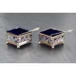 A pair of Edwardian silver salts of diamond form having pierced decoration, blue golass liners and