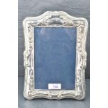 A modern silver photograph frame having moulded scroll decoration with plain cartouche and black