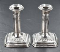 A pair of George V silver candlesticks, with ribbon, pendant and swag decoration over a stepped