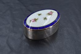 An early 20th Century silver trinket box of plain oval form having enamelled lid with rose