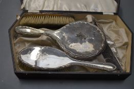 A case containing a selection of HM silver dressing table items, most damaged