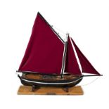 A PAINTED TIMBER MODEL OF A GALWAY HOOKER, with traditional red sails, on a timber stand.