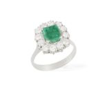 AN EMERALD AND DIAMOND CLUSTER RING, the rectangular-cut emerald within a four-claw setting with a