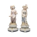 A PAIR OF CONTINENTAL POLYCHROME BISQUE FIGURES, of seated maidens with attendant winged putti,