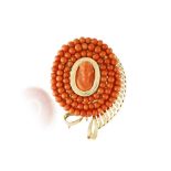 A CORAL BROOCH, CIRCA 1960, the central corallium rubrum coral cameo, within a surround of