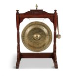 AN EDWARDIAN STAINED OAK AND BRASS DINNER GONG AND BEATER, of architectural form,