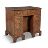 A GEORGE II WALNUT KNEEHOLE DESK, the quarter veneered cross banded top above a single frieze