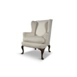 A GEORGIAN STYLE WALNUT FRAMED WING BACK ARMCHAIR upholstered in cream raised on shell capped