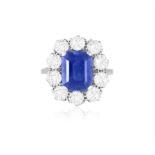 A SAPPHIRE AND DIAMOND CLUSTER RING The cut-cornered rectangular sapphire weighing approximately