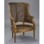 A Louis XVI style carved giltwood frame bergere with rounded cane-panel back, scroll arms, cane seat