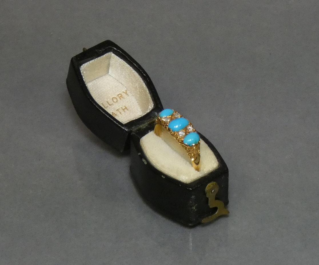 A late Victorian gold ring set three graduated turquoise cabochons with pairs of small diamonds in