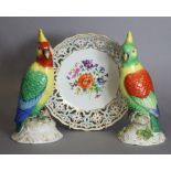 A pair of continental porcelain models of parrots, each sat on rocky leaf-encrusted base, 9.75”
