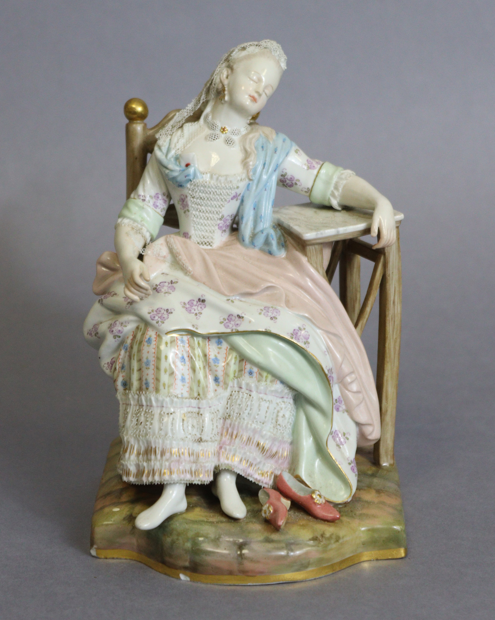 A Meissen figure of a lady asleep in a chair, one arm resting on a marble-top table, blue crossed