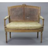 A 19th century French carved beech frame small sofa in the Louis XVI style, with curved cane-panel