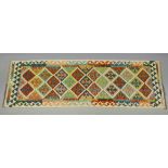 A Choli kilim runner of ivory ground with multi-coloured repeating lozenge design within a wide