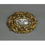 A mid-19th century yellow metal oval mourning brooch of embossed scroll design with central hair