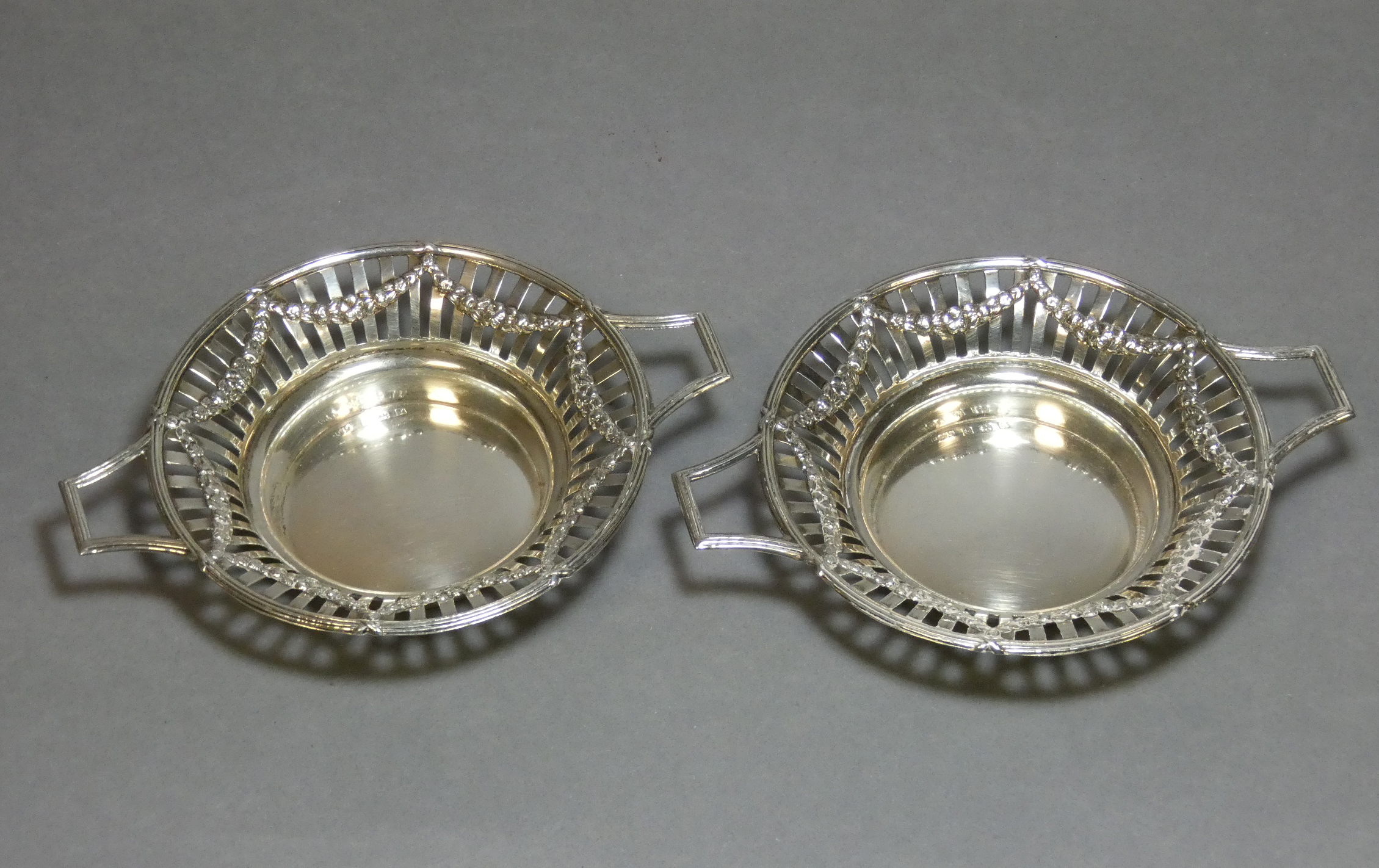 A pair of Edwardian silver circular two-handled sweetmeat dishes with embossed swags to the