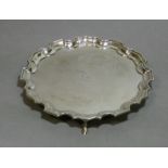 An Edwardian silver circular waiter with raised pie-crust border, engraved crest to centre, on three