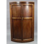 A walnut tall standing bow-front corner cupboard fitted two shelves enclosed by a pair of panel