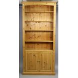 A pine tall standing open bookcase with five adjustable open shelves above a cupboard enclosed by