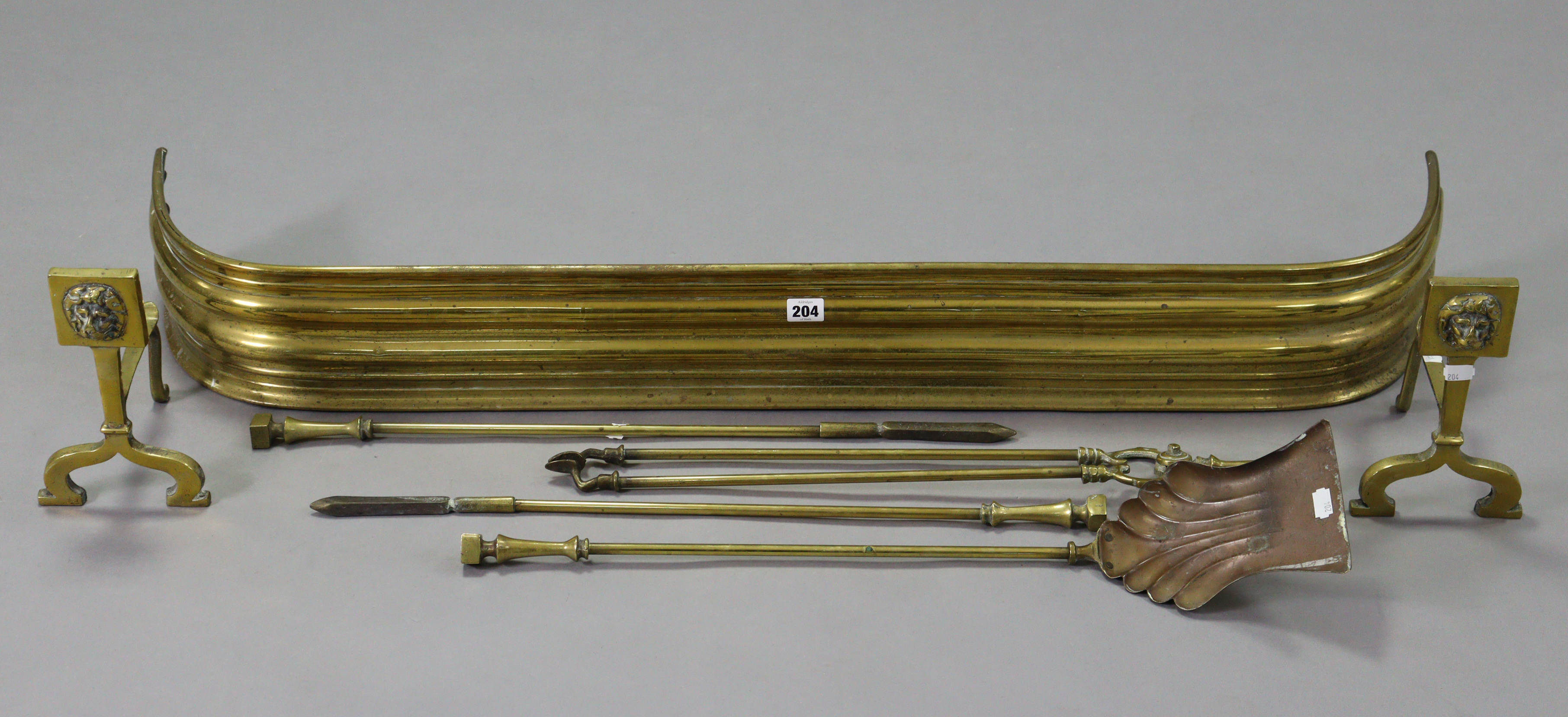 A brass fender, 45” long; together with a pair of brass fire dogs; & a set of four brass fire