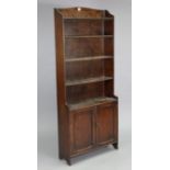 An early 20th century oak standing bookcase fitted five open shelves above a cupboard enclosed by