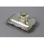 A George V silver desk inkstand with shaped border, pen-trough to one side, fitted square glass