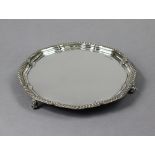 A silver circular salver with shaped raised border & gadrooned rim, on three short leaf-scroll feet,