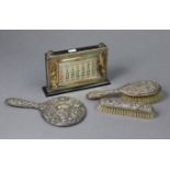 A hand mirror, clothes brush, & hair brush with embossed silver backs, Birmingham 1955; & a silver-