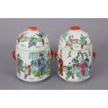 A pair of Chinese porcelain cylindrical jars & covers, decorated with figure scenes in famille verte