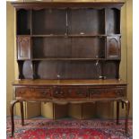 An 18th century oak dresser with open shelves above, fitted two small cupboards, the base fitted