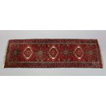 A Persian corridor runner of madder ground with repeating geometric floral design within narrow