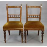 A pair of late Victorian carved walnut rail-back dining chairs with padded seats, & on turned legs,