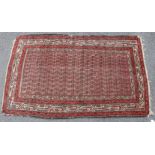A Persian rug of madder ground with repeating geometric design to the centre surrounded by