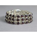 A silver flexible bracelet of three rows set amethyst-coloured cabochons.