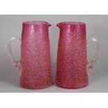 A pair of cranberry glass ‘crizzled’ jugs, each with clear reeded & flared scroll handle, 10¼”