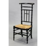 A French ebonised wooden chapel chair with a woven rush seat, & on bobbin-turned supports.