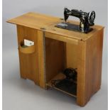 A Singer electric treadle sewing machine in an oak case enclosed by a hinged lift-lid & a panel