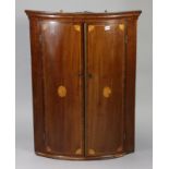 A 19th century inlaid-mahogany bow-front hanging corner cupboard fitted two shelves enclosed by a