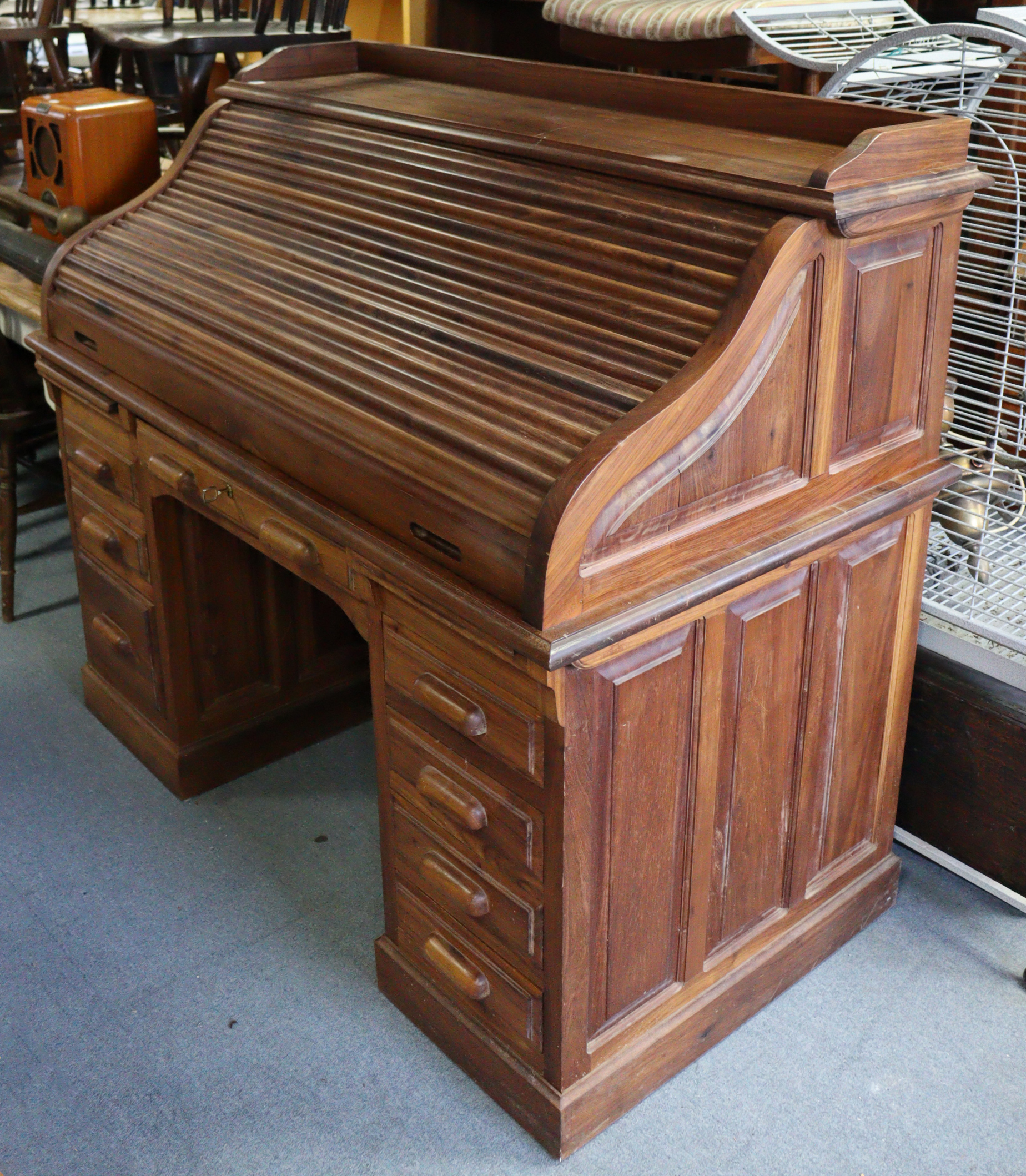 A teak roll-top desk with a fitted interior enclosed by a tambour shutter, & fitted four long