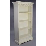 A white-finish tall standing open bookcase with a pierced frieze, fitted three shelves above two